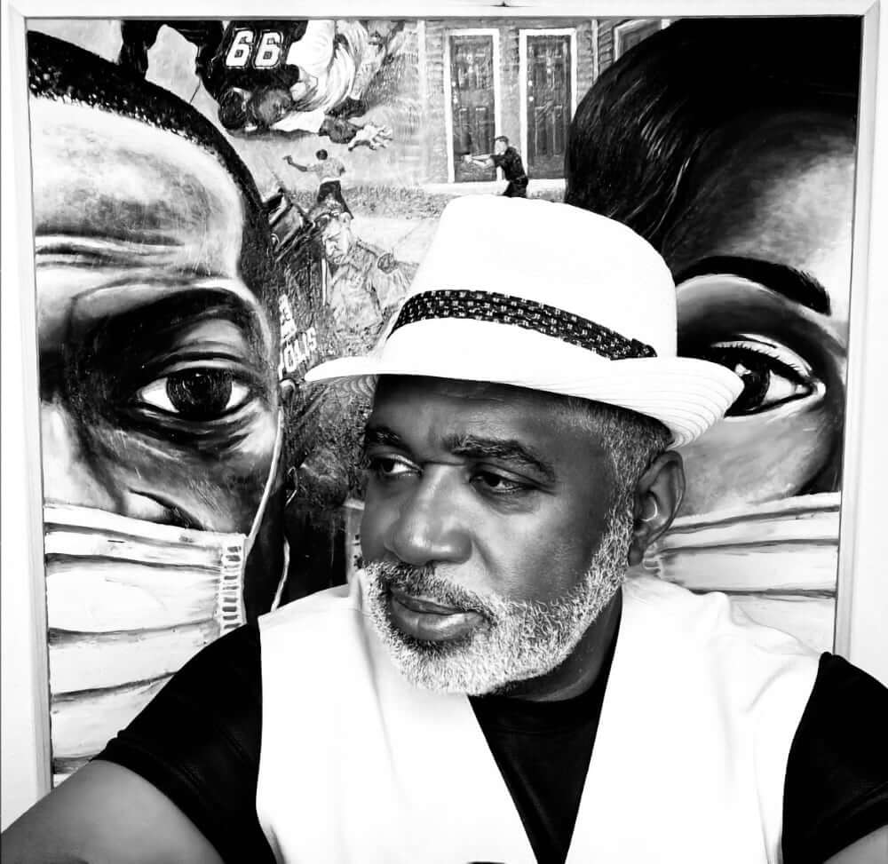 Antoine Prince A black and white image of a dark-skinned African American man with a mingled gray beard wearing a white hat with a black hatband, a white suit vest, and a black t-shirt. He is in a three-quarter pose in front of a painting entitled, "Why I Can't Breathe."