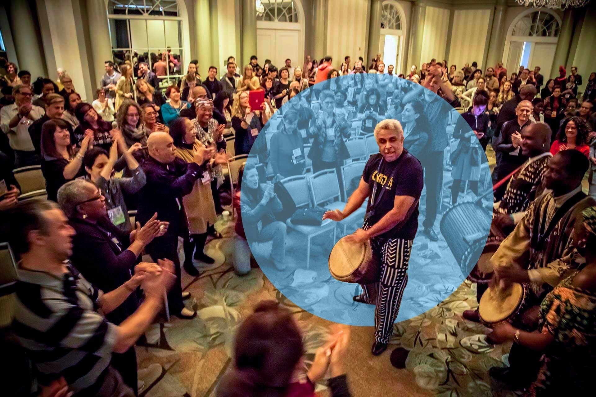 A lively crowd surrounds a group of drummers in a grand ballroom, clapping and dancing with joy. One central drummer, Luther Gray, wearing patterned pants and a “Civica” shirt, is highlighted by a blue circular overlay that isolates him visually from the rest of the room. The atmosphere is energetic and festive, with people fully engaged in the rhythm and performance.