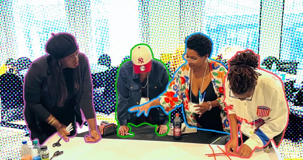 A stylized photograph of four Black women standing at a table and engaged in a brainstorming or team building activity. The background of the photo has a halftone treatment that separates it from the figures in the foreground. Each of the four women is outlined in a different color border. Starting from the left, the first woman has long straight black hair, and she is leaning over the table and looking to her left at the the third woman. She is dressed in black pants and shirt with a fitted black blazer, and wearing a black beret. She is outlined in purple. The next woman is wearing a white and red New York Mets baseball cap and blue denim jacket, and she has her head down and both hands placed on the table. She is outlined in green. The third woman wears glasses and has closely cropped hair, and she is extended her right hand as she explains something, while holding a bundle of white pens with blue caps in her left hand. She is wearing a v-cut blouse and a white jacket covered in large red, orange, and blue flowers and green leaves. She is outlined in blue. The fourth woman wears glasses and has her hair pulled back in a loose bun. She is wearing a loose fitting white long-sleeved shirt with a pocket that looks like a stylized recreation of the U.S. flag turned so that the blue section with stars is at the top and the stripes run vertically. There is a red band on the right sleeve near the wrist, and a blue band on the left sleeve near the wrist. She is looking down and arranging red pipe cleaners or strips of paper on the table. She is outlined in red.
