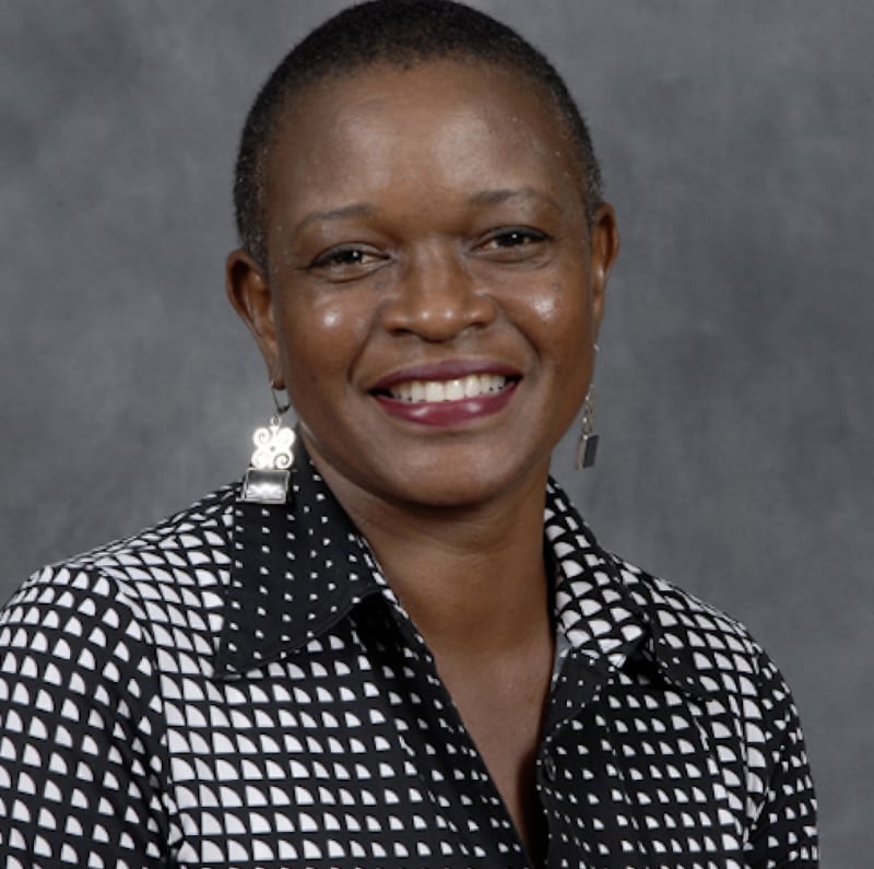 Sheleen Jones The photo shows a dark-skinned African American woman with short-cropped, natural hair. She is wearing a black-and-white buttoned shirt and silver earrings and smiling broadly at the camera.