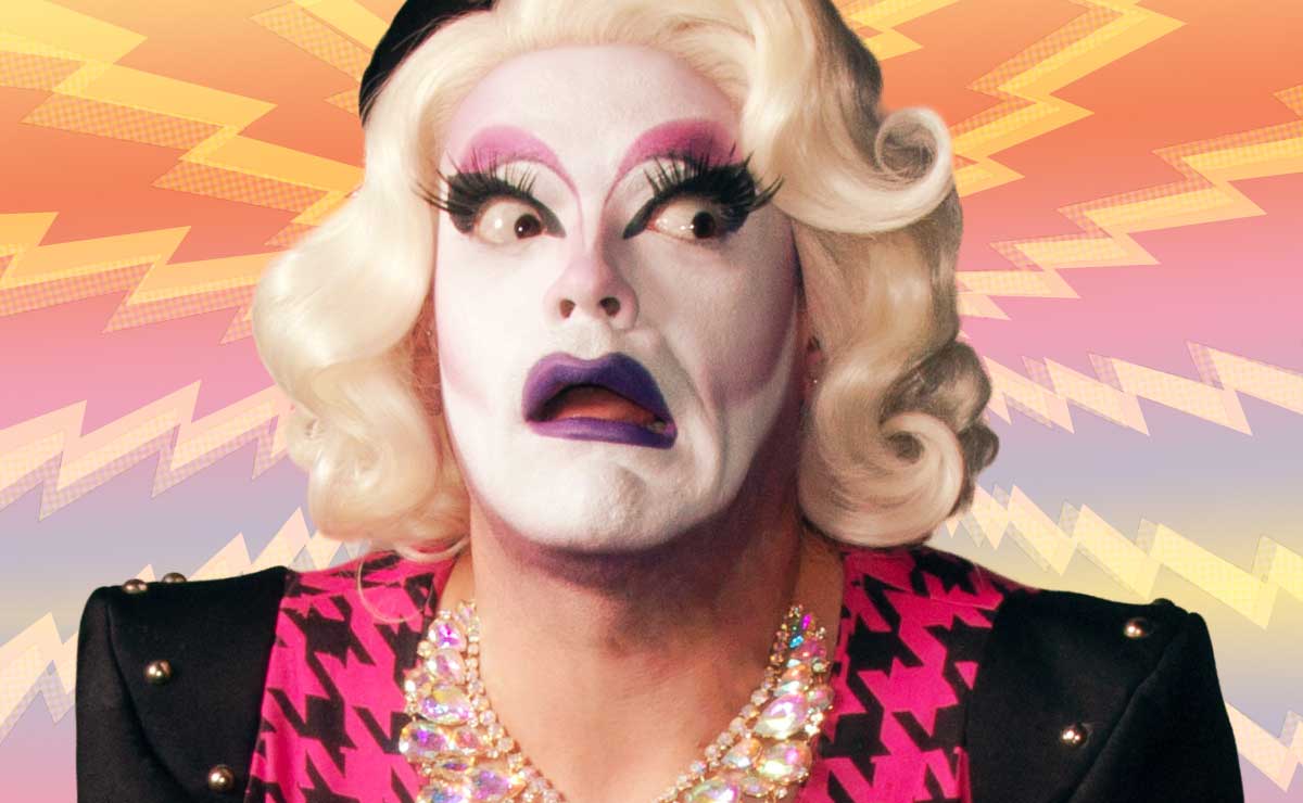 Drag performer Carla Rossi, wearing a bold makeup look featuring black, smoky eyes, purple lipstick, and a shoulder length blond wig.