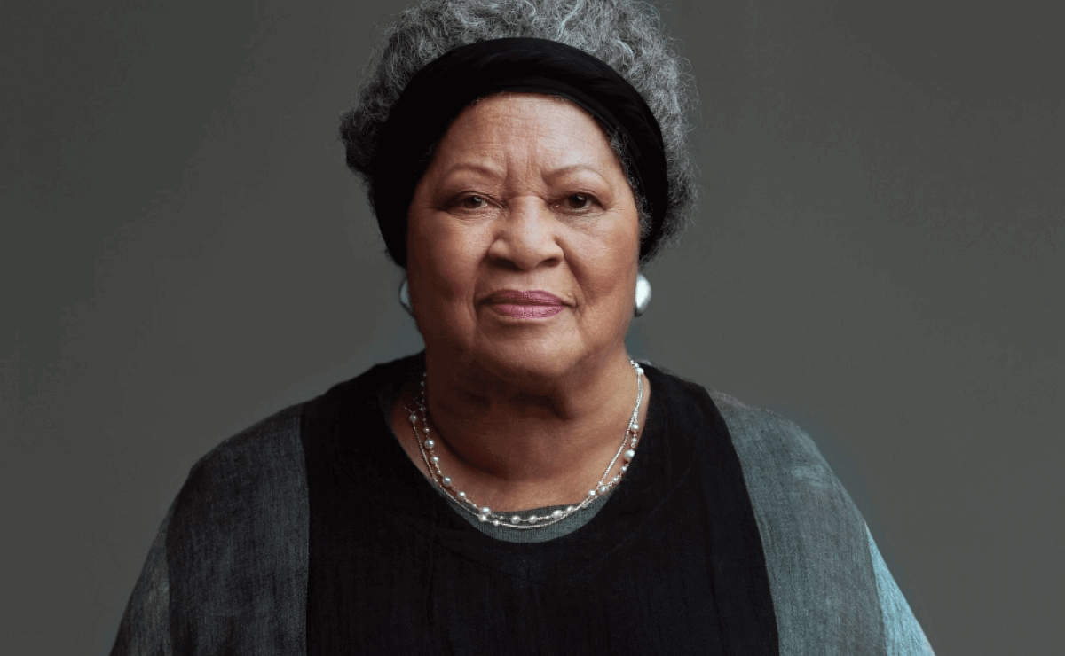 Portrait of Toni Morrison, wearing a gray and black dress and a black partial head wrap, staring directly at the viewer.