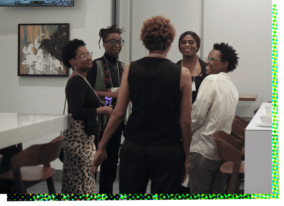 Five Black women stand in a group laughing and talking. Starting from the left, the first woman, Keana Brewster, wears glasses and has short black hair, and she is wearing a leopard print long skirt and a black blouse. The second woman, Kerrigan Casey, has medium-length black hair pulled up on top of her head and wears glasses. She appears to be wearing a faded blue vest over a black shirt. The third woman has her back to the camera, but is identified as Stephanie Atkins. She has short reddish hair and is wearing a sleeveless black top and black pants. The fourth woman, Simone Immanuel, has long black hair pulled back in a ponytail and is wearing a black dress. The fifth woman, Jazz Franklin, has short spiky hair and wears glasses. She is wearing a loose fitting, untucked white long sleeved shirt.
